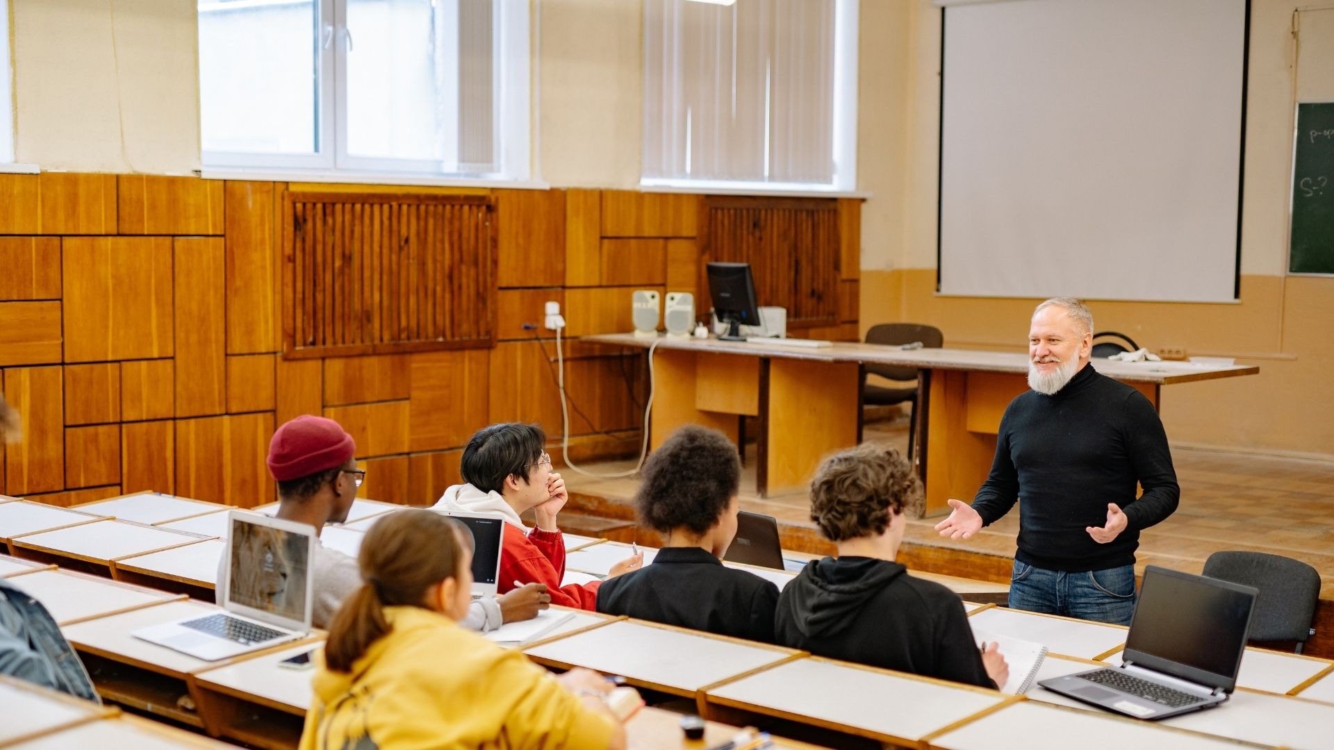 A lecturer teaching a small class of masters students with laptops